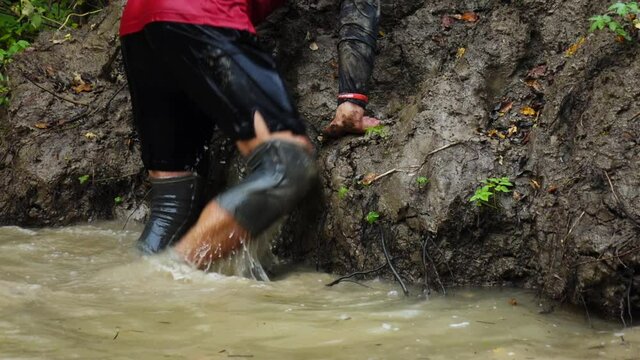 Overcome obstacle courses in water and mud. Participants make their way through a ditch during the race. Slow motion