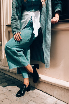 Woman In A Red Stylish Suede Loafer Shoes, Blue Jeanse, White Shirt And Trendy Checkered Coat Posing On The Street. Pair Of Trendy Female Loafers Shoes.