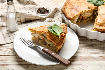 Baking dish and plate with piece of tasty chicken pot pie on white wooden background