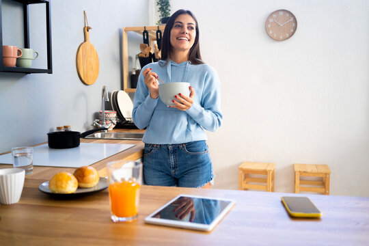 Smiling Young Woman Holding Bowl By Kitchen Counter At Home