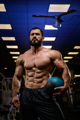 Fototapeta na wymiar strong young bearded caucasian athlete with medicine heavy ball in blue lit night sport gym