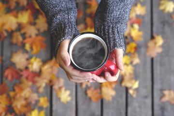 Autumn drink tea or coffee in hands on the background of October yellow leaves. Autumn comfort and...