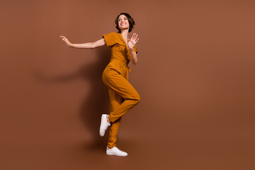 Fototapeta na wymiar Full length photo of cheerful positive cool young woman dance wear look empty space isolated on brown color background
