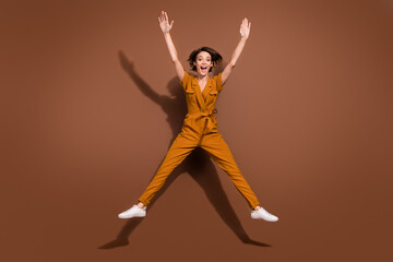 Fototapeta na wymiar Full body photo of amazed cheerful young happy woman raise hands jump up good mood isolated on brown color background