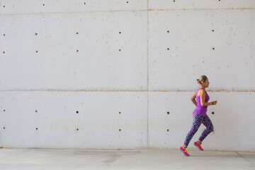 Fototapeta na wymiar Sporty Woman. Beautiful Woman Running In The City Next To Buildings With Modern Architecture . Fitness, Workout, Sport, Lifestyle Concept.
