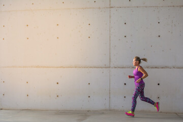 Sporty Woman. 
Beautiful Woman Running In The City Next To Buildings With Modern Architecture . Fitness, Workout, Sport, Lifestyle Concept.
