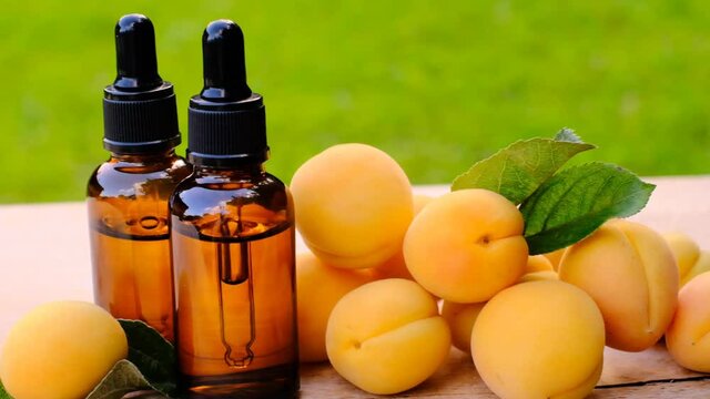 Apricot kernel oil in a glass bottle with a pipette and ripe apricots fruits on a wooden table on a blurred green garden background. Organic natural bio oil. Apricot oil