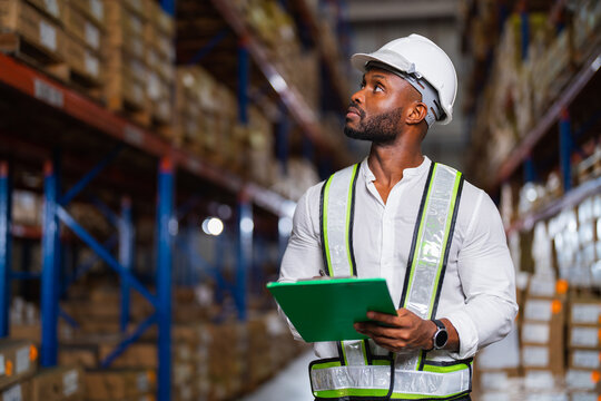 Portrait of an African warehouse manager holding a clipboard checking inventory in a large distribution center.