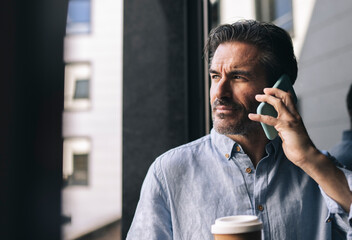 Male professional talking on mobile phone while having coffee at hotel room