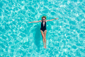 Top view aerial of a seductive sexy model in black swimwear is enjoying relax in turquoise sea summer weekend. Tropical background with empty space.