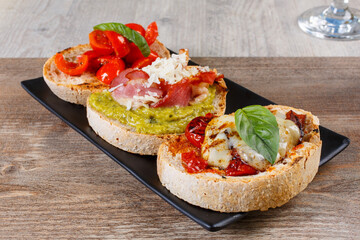 Bruschette di pane arrostite sulla brace con pesto di basilico, speck, pomodori, basilico fresco, pomodori secchi e provola affumicata