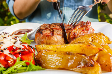 Filetto di carne con contorno di patate al forno, pomodori, rucola, formaggio e olio balsamico mentre viene tagliato con forchetta e coltello