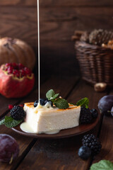A square piece of cottage cheese casserole lies on a plate, decorated with berries and mint leaves. Condensed milk is poured on top of the omelet