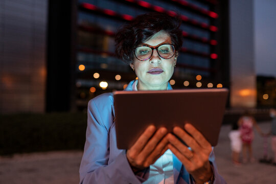 Female professional wearing eyeglasses using digital tablet at night - Powered by Adobe