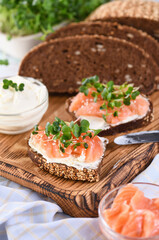 Open sandwich with cheese cream on a slice of rye bread with cereals, slices of marinated salmon, and radish sprouts.