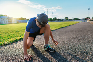 concept of sports and health - teen boy posing at a stadium track, he ties his shoelaces, a soccer...