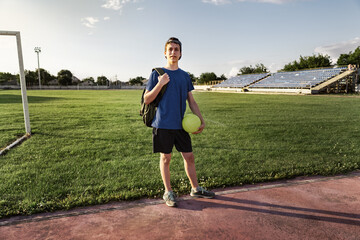 concept of sports and health - teen boy posing at a stadium, a soccer field with green grass.