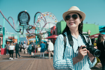 Fototapeta premium Photographer girl with lens camera. woman tourist enjoy summer vacation outdoors takes pictures in amusement park. joyful female professional photographer relax with bokeh view ferris wheel in back
