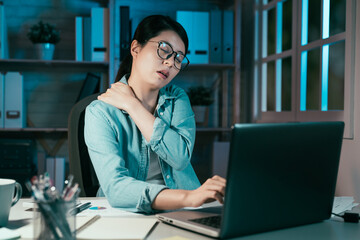 Tired asian chinese businesswoman feeling neck pain working on laptop at night in modern home...