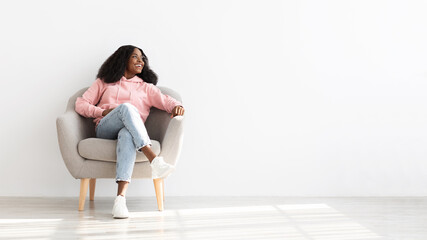 Cheerful black woman posing resting in arm chair at home