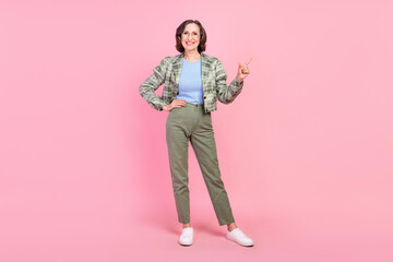 Fototapeta premium Full length photo of cheerful old woman point finger empty space news garage sale clothes isolated on pastel pink color background