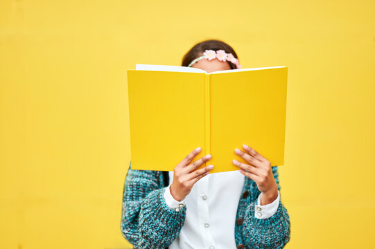 Young woman reading yellow book by wall