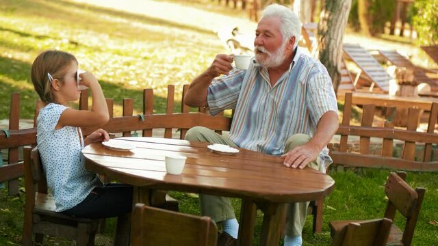 Grandfather and little girl playing to drink coffee sitting on a small children's wooden table in the yard