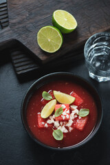 Black bowl with gazpacho cold soup made of watermelon, high angle view on a black stone surface, vertical shot
