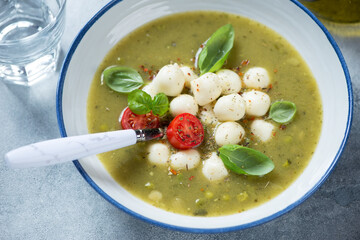 Close-up of vegetable soup with green peas, spinach, leek, scamorza cheese and green basil, selective focus, studio shot