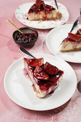 A piece of cake on a white plate on a pink surface: no bake cheesecake with dark red jelly and fig slices