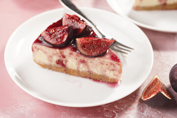 A piece of cake on a white plate on a pink surface: no bake cheesecake with dark red jelly and fig slices