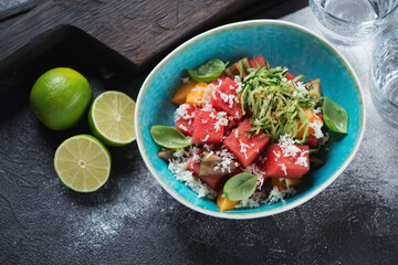 Watermelon, tomato, bryndza and cucumber salad served in a turquoise bowl, elevated view on a dark grey stone background