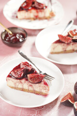 A piece of cake on a white plate on a pink surface: no bake cheesecake with dark red jelly and fig slices
