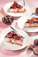 A piece of cake on a white plate on a pink surface: no bake cheesecake with dark red jelly and fig slices