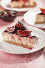 A piece of cake on a white plate on a pink surface: no bake cheesecake with dark red jelly and fig slices