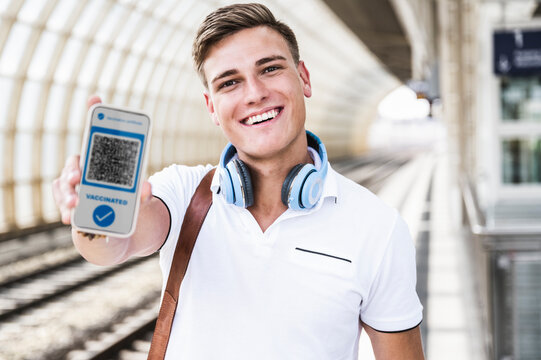 Smiling man wearing headphones holding mobile phone with vaccination certificate at subway