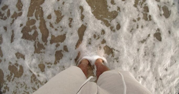 Caucasian male standing on beach with feet in the water 