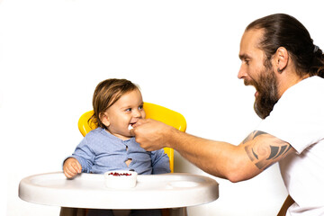 Dad laughs and feeds the baby on on the highchair. The concept of spending time with children.Front view photo on a light background. Life style