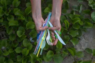 Hands holding used plastic dishes and straws on the beach. Beautiful green grass on the background....