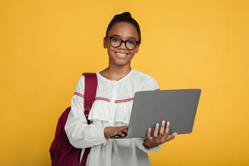 Smiling smart cute teenage african american girl pupil in glasses with backpack studying with laptop