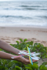 Fototapeta na wymiar Hands holding used plastic dishes and straws on the beach. Clean ocean beach and green grass on the background. Plastic pollution, Environmental. 
