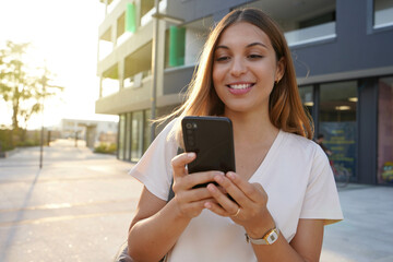 Young attractive woman using smartphone in city at sunset - obrazy, fototapety, plakaty
