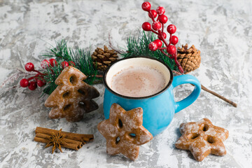 A cup with aromatic cocoa, cinnamon, star anise, gingerbread and Christmas decor on a light tabletop