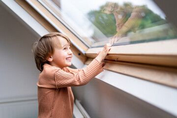 Close up portrait of a little preschool boy looking at the window and laughing. Happy smiling child spends time at home alone.
