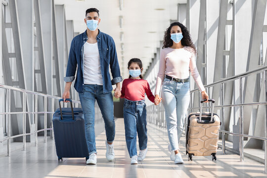 Middle-Eastern Family Of Three Wearing Medical Masks Walking With Luggage In Airport