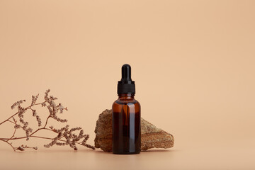 Skin serum bottle next to natural stone and dry flower against beige background with copy space - obrazy, fototapety, plakaty