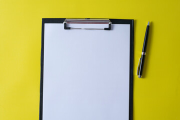 Top view of blank paper on clipboard on yellow background and different objects. Minimal flat lay style.