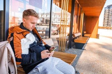 A young man uses a smartphone while sitting at a bus stop. A business man is waiting for a bus at a...