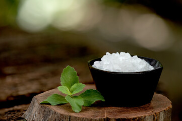 Saccharin or sweetener crystals and stevia branch green leaves on an old wood background.