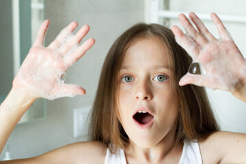 Happy smiling girl having fun with soap bubble in lockdow. COVID-19 Coronavirus prevention washing hands with soap at bathroom.